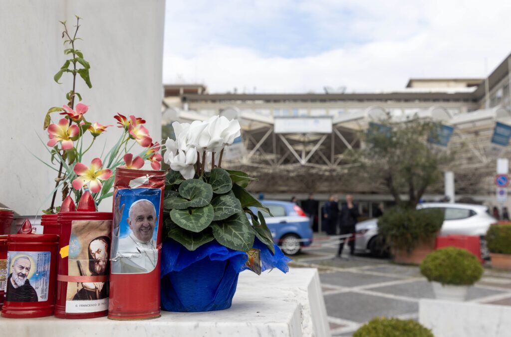 Flores y velas votivas en la base de una estatua de San Juan Pablo II frente al hospital Gemelli de Roma el 18 de febrero de 2025, donde el Papa Francisco está hospitalizado. (Foto CNS/Pablo Esparza)