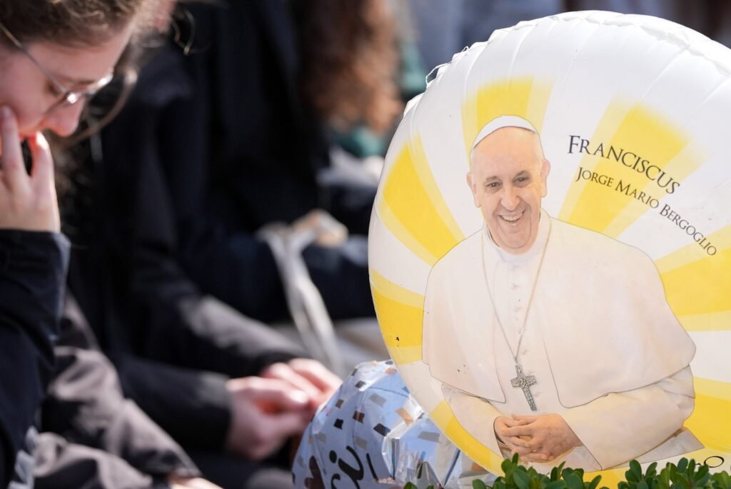 Un globo con una imagen del Papa Francisco es visto mientras la gente reza alrededor de una estatua de San Juan Pablo II fuera del hospital Gemelli de Roma el 2 de marzo de 2025. El Papa Francisco está recibiendo tratamiento allí por una neumonía doble. (Foto CNS/Lola Gomez)