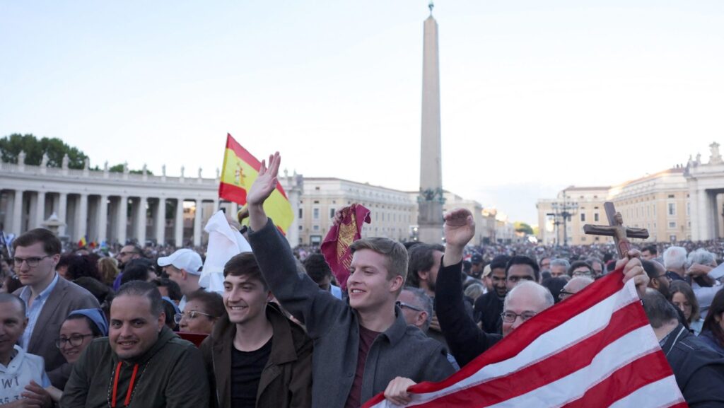 Hombres con una bandera estadounidense celebran mientras el cardenal Robert Francis Prevost —ahora Papa León XIV— aparece en el balcón central de la Basílica de San Pedro en el Vaticano el 8 de mayo de 2025, tras ser elegido durante el cónclave. Es el primer papa estadounidense en la historia. (OSV News/Amanda Perobelli, Reuters)