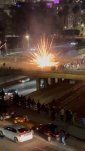 Una imagen tomada de un video desde una ventana de la residencia de la catedral la noche del 8 de junio muestra lo que parece ser un fuego artificial explotando frente a los policías en el puente de Broadway sobre la autopista 101. Se puede ver a una multitud observando desde el puente de Hill Street. (Padre Matthew Wheeler)