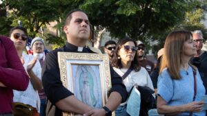 El padre Peter Saucedo sostiene un cuadro de Nuestra Señora de Guadalupe mientras escucha a los oradores en una vigilia interreligiosa el 10 de junio en Grand Park, en el centro de Los Ángeles, a pocas cuadras de la catedral. (Kimmy Chacón)