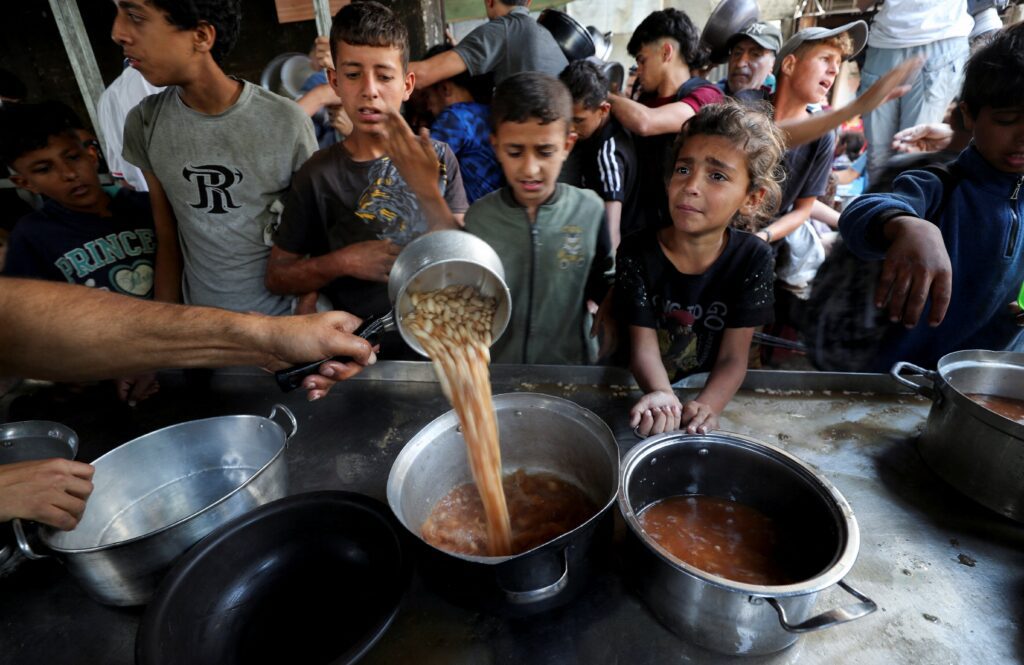 Jóvenes palestinos desplazados por la ofensiva militar israelí reaccionan el 21 de mayo de 2025, mientras esperan recibir alimentos cocinados por una cocina benéfica en la ciudad de Gaza, Franja de Gaza. (Foto de OSV News/Mahmoud Issa, Reuters)