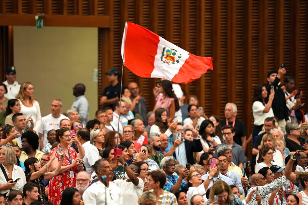 Peregrinos izan la bandera de Perú cuando el Papa León XIV llega a la Sala de Audiencias Pablo VI en el Vaticano para su audiencia general el 13 de agosto de 2025. (Foto CNS/Lola Gómez)