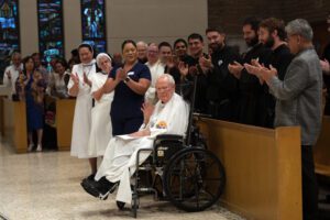 El padre Jim Mott, un párroco de larga trayectoria en la iglesia Our Mother of Good Counsel en Los Feliz, saluda al público al recibir una ovación de pie durante la Misa especial por el centenario de la parroquia, el 6 de septiembre. (Bernard Ejada)
