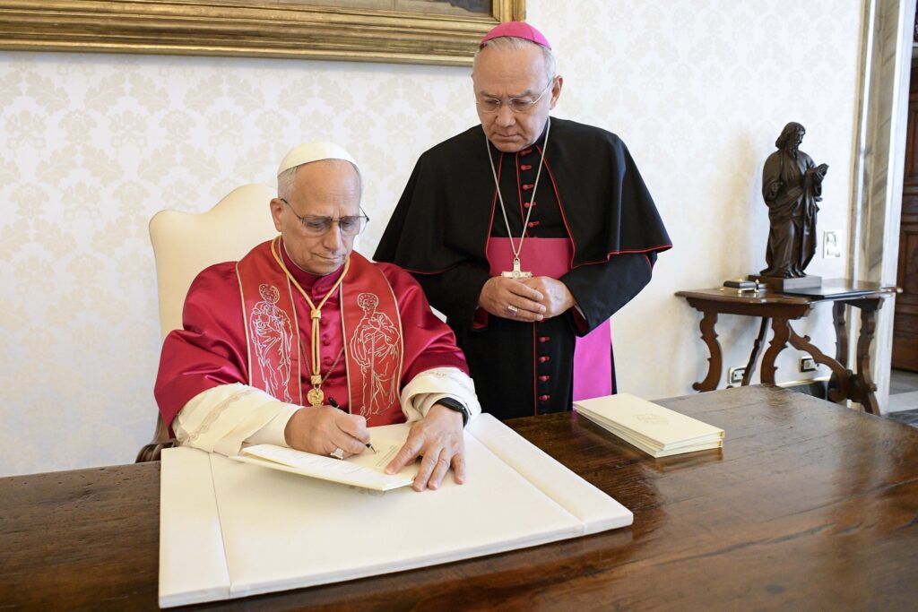 El papa León XIV firma su primera exhortación apostólica, «Dilexi Te» («Te he amado»), en la biblioteca del Palacio Apostólico del Vaticano el 4 de octubre de 2025, festividad de San Francisco de Asís, en presencia del arzobispo Edgar Peña Parra, secretario sustituto para los asuntos generales de la Secretaría de Estado del Vaticano. La exhortación se publicó el 9 de octubre. (Foto CNS/Vatican Media)