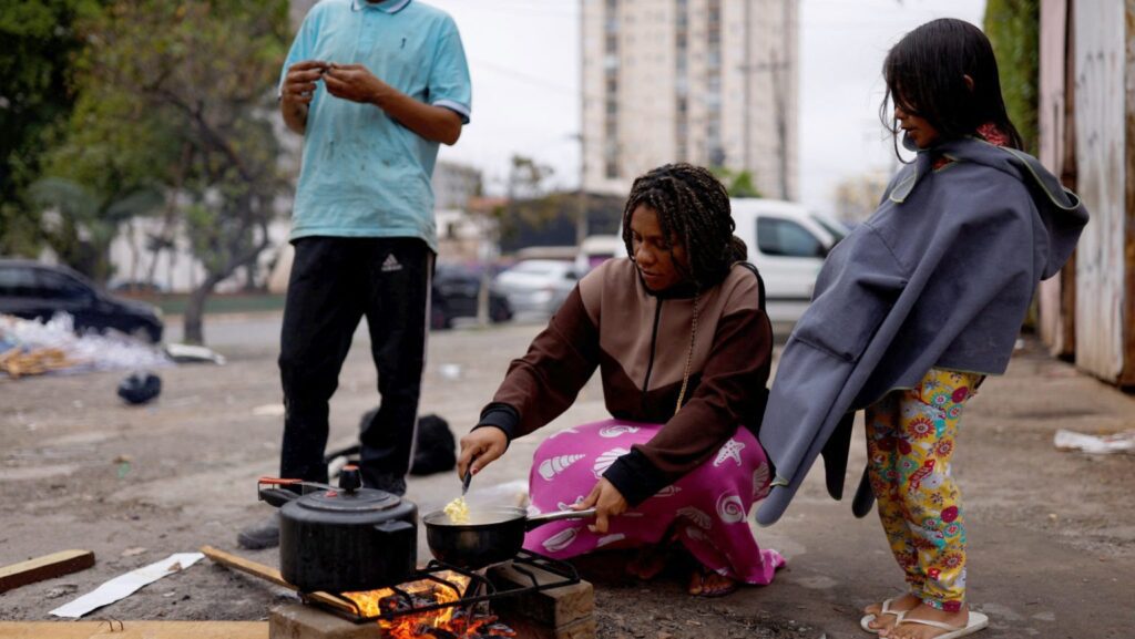 Una mujer quema leña en la calle para cocinar una comida para su esposo y su hija frente a su casa en São Paulo en 2022. (OSV News/Amanda Perobelli, Reuters)