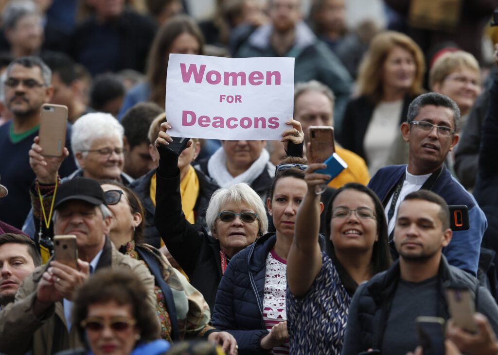 Una mujer sostiene un cartel en apoyo a las mujeres diáconas mientras el papa Francisco dirige su audiencia general en la plaza de San Pedro del Vaticano el 6 de noviembre de 2019. (Foto CNS/Paul Haring)