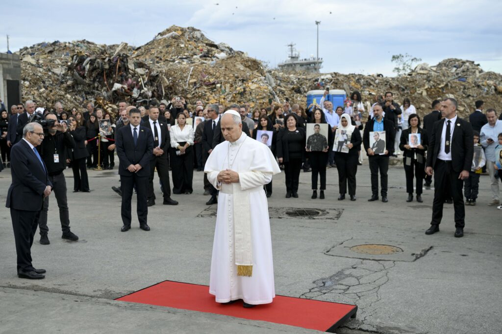 De pie entre los escombros y con los familiares de las víctimas mortales detrás de él, el papa León XIV reza ante un monumento conmemorativo que marca el lugar donde se produjo una mortal explosión en 2020 en el puerto de Beirut, el 2 de diciembre de 2025. (Foto CNS/Vatican Media)