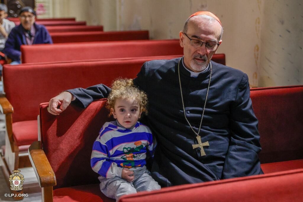 El cardenal Pierbattista Pizzaballa, patriarca latino de Jerusalén, reza junto a un niño en un banco de la iglesia de la Sagrada Familia en la ciudad de Gaza el 20 de diciembre de 2025, durante su visita pastoral navideña. Llegó antes de Navidad en señal de cercanía con una comunidad que ha soportado dos años de guerra. (OSV News/cortesía del Patriarcado Latino de Jerusalén)