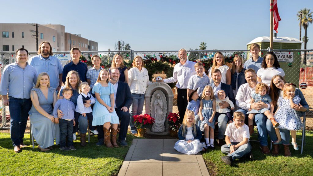 Jackie y Peter Halpin, en el centro, posan con sus hijos, nueras, yernos y nietos — junto a la estatua de la Virgen María que sobrevivió al incendio — después de la bendición de su terreno y de la casa en reconstrucción en Altadena, el 13 de diciembre de 2025. (Foto enviada)