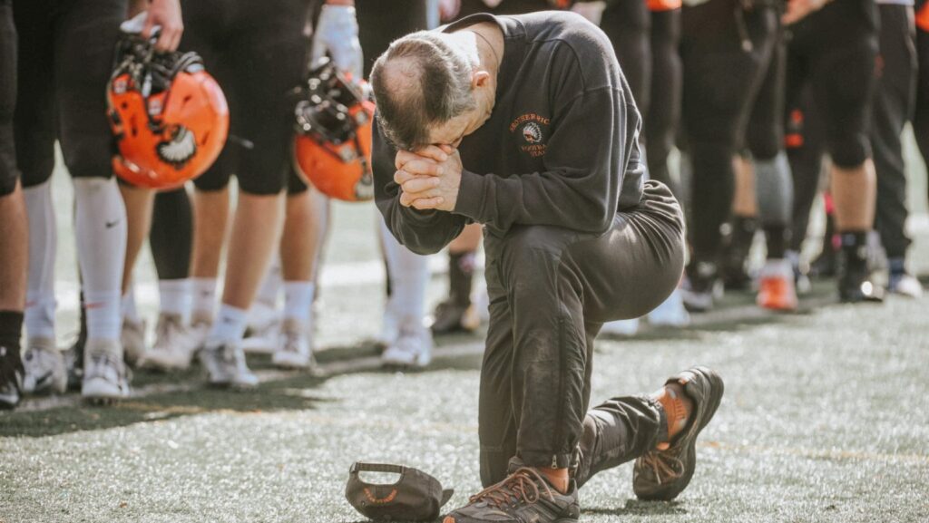 Un entrenador se arrodilla en oración el 13 de octubre de 2018 durante un partido de secundaria en Hurley Field en Berkeley, Michigan. Los obispos de EE.UU. han emitido un nuevo informe sobre cuestiones de libertad religiosa en el país y cómo la Iglesia católica se ha visto afectada. (Foto OSV News/Tim Fuller, cortesía de la Arquidiócesis de Detroit)