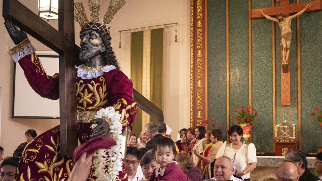 Tharese Carpio, al centro, es alzada para recibir una bendición ante la nueva estatua del Nazareno Negro en Holy Family Church en Artesia el 14 de febrero. (Juanito Holandez Jr.)