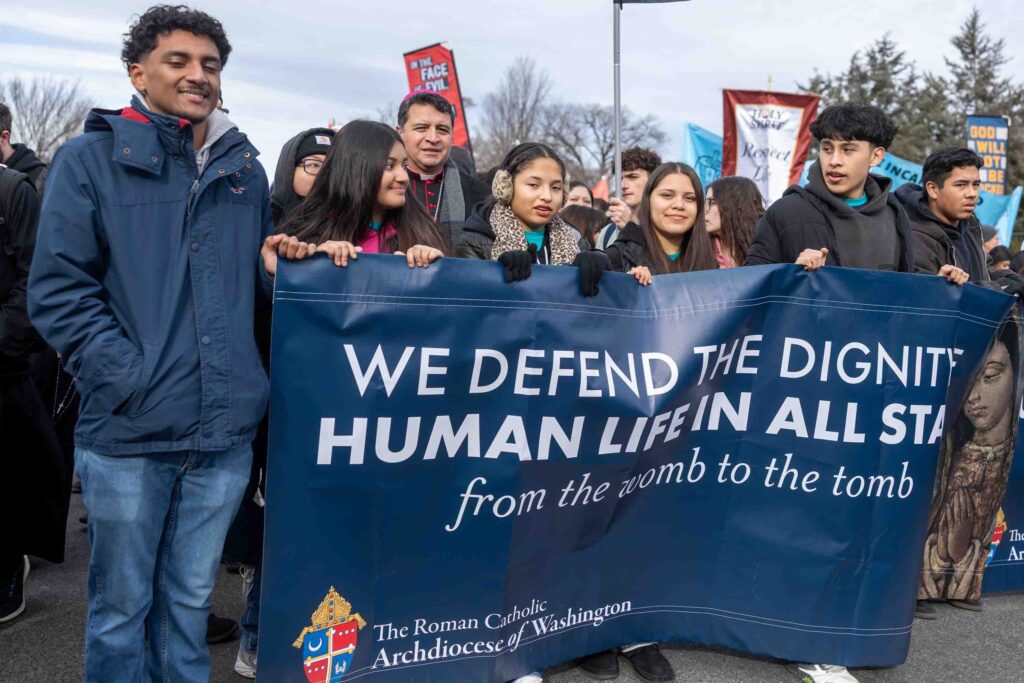 Acompañados por el obispo auxiliar de Washington, Evelio Menjívar (centro, atrás), jóvenes católicos caminan en la Marcha por la Vida el 23 de enero del 2026 desde el Mall hasta la Corte Suprema de Justicia portando su consigna en una gran pancarta que reza: Defendemos la dignidad de la vida humana en todas sus etapas. Según un análisis de datos realizado por Mark Gray del Centro de Investigación Aplicada para el Apostolado (CARA, por sus siglas en inglés) y publicado el 23 de marzo de 2026, los adultos católicos más jóvenes en EE.UU. son más propensos a ser hispanos o latinos, mientras que poco más de la mitad de los individuos de la Generación Z criados como católicos probablemente mantengan esa identidad en la edad adulta. (Foto OSV News/Mihoko Owada, El Pregonero)