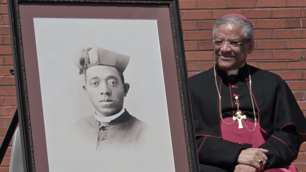 El obispo auxiliar emérito de Chicago, Joseph N. Perry, se encuentra junto a un retrato del primer sacerdote afroamericano de Estados Unidos, el padre Augustus (Agustín) Tolton, durante el anuncio del 29 de abril de 2026 sobre el santuario previsto en su honor en la iglesia de San Bonifacio, en Quincy, Illinois. (Foto OSV News/cortesía de la Diócesis de Springfield)