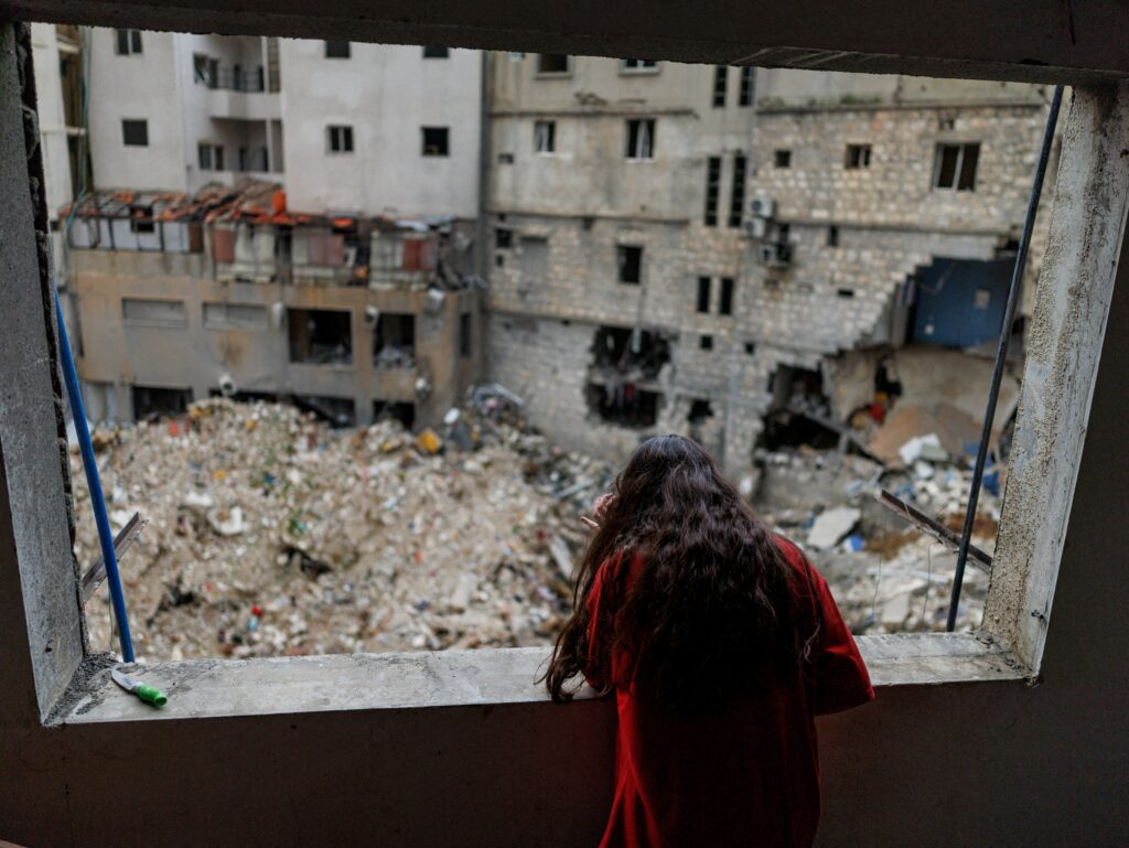 Alaa Dahnoun, de 12 años, quien dijo que sobrevivió a un ataque israelí que la obligó a huir con sus padres a Beirut, mira a través de la ventana dañada de su apartamento en Nabatieh, Líbano, el 18 de abril de 2026, después de que entrara en vigor un alto el fuego de 10 días entre Líbano e Israel. (Foto OSV News/Zohra Bensemra, Reuters)