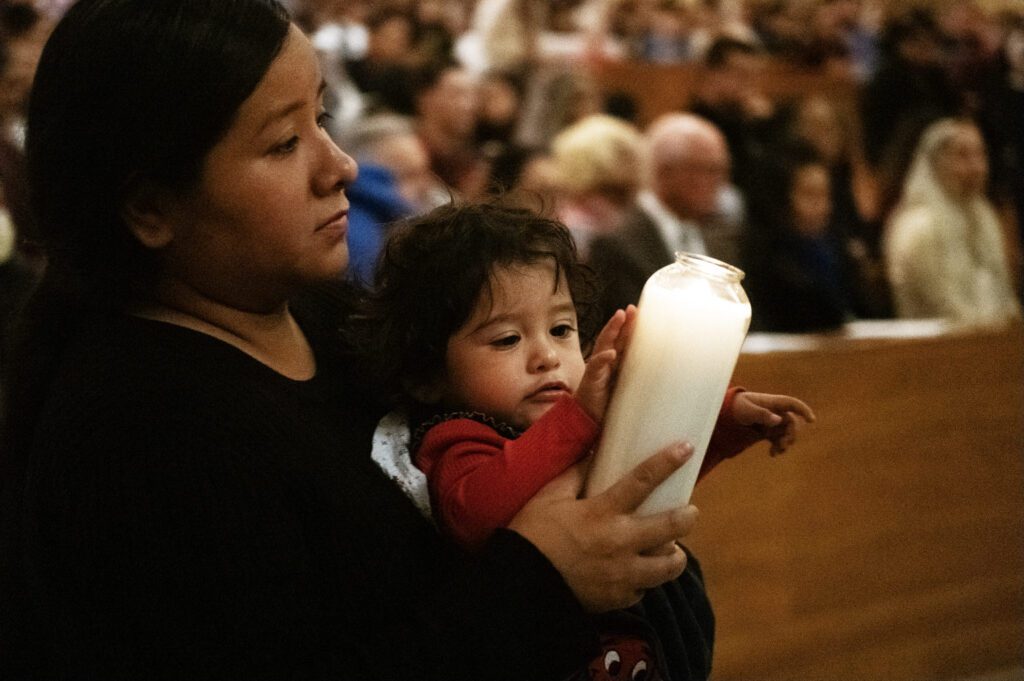 Una mujer sostiene a un niño pequeño y una vela durante la Misa de Réquiem por los No Nacidos de la Arquidiócesis de Los Ángeles en 2025. (Victor Alemán)