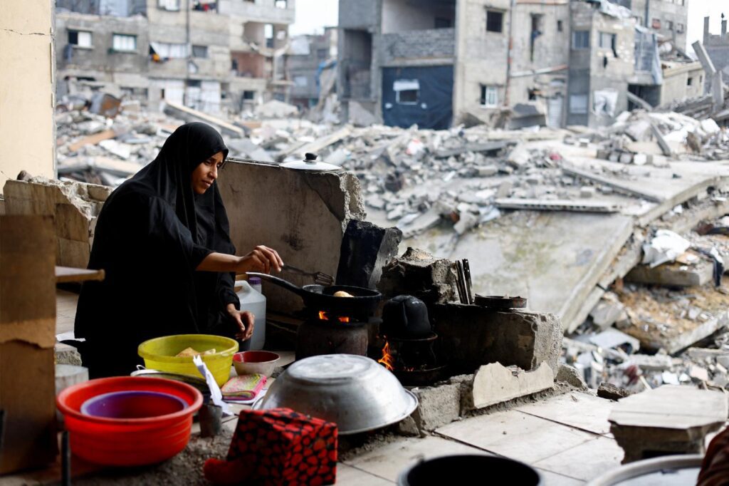 Una mujer palestina cocina en Jabalia, al norte de la Franja de Gaza, el 31 de diciembre de 2025. Al fondo se observan los restos de edificios residenciales destruidos durante la guerra. Un día antes, Israel anunció la suspensión de las operaciones de más de dos decenas de organizaciones humanitarias, entre ellas Cáritas. (OSV News foto/Mahmoud Issa, Reuters)