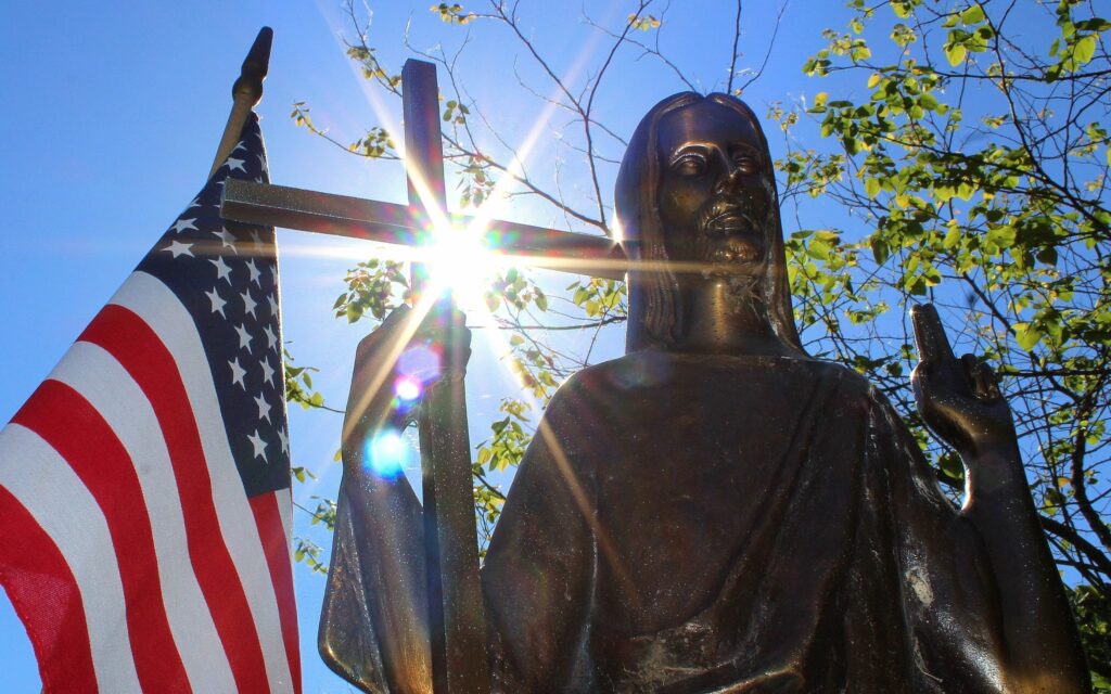 La luz del sol ilumina una estatua de Cristo sobre una lápida junto a una bandera estadounidense en el cementerio católico St. Mary de Appleton, Wisconsin, en esta imagen de 2018. La Semana de la Libertad Religiosa 2026, organizada por la Conferencia de Obispos Católicos de Estados Unidos, tendrá lugar del 22 al 29 de junio y es más relevante que nunca, afirmó Emily Schumacher-Novak, del Secretariado de Justicia y Paz de la USCCB. (Foto de archivo OSV News/Bradley Birkholz).