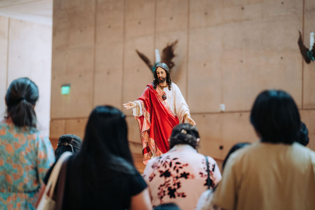 performer dressed as Jesus in white and red robes speaks to a seated audience in a large hall.