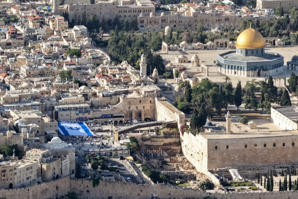 Aerial view of Jerusalem's Old City showing the gold Dome of the Rock, stone buildings, and a large crowd around the Western Wall area.