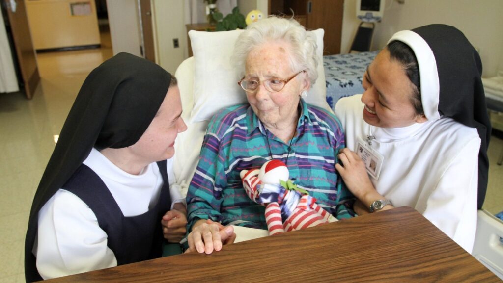 Una foto de archivo muestra a la postulante dominica Anna Harper, originaria de Baton Rouge, Luisiana, y a la hermana dominica Carmela Marie, originaria de Hinatuan, Filipinas, durante una visita a la paciente Edna MacCready en el Hogar Rosary Hill, en Hawthorne, Nueva York. Cuatro congregaciones de religiosas y ministerios católicos de atención médica presentaron una demanda ante un tribunal federal en Albany el 17 de julio de 2026, al argumentar que la nueva ley de Nueva York sobre el suicidio asistido las obligaría a elegir entre su fe y su capacidad para brindar atención a los enfermos, los ancianos y las personas al final de la vida. (Foto de OSV News/Gregory A. Shemitz)