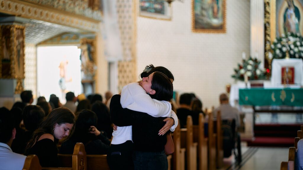 Dos mujeres se abrazan antes de la misa especial celebrada el 28 de junio de 2026 en la iglesia Nuestra Señora de Guadalupe, en el este de Los Ángeles, para orar por las víctimas de los terremotos en Venezuela. (John Geronilla)