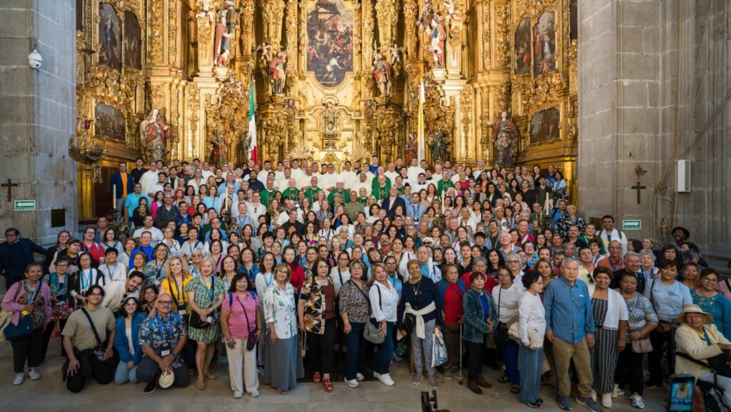 Large diverse group posing for a photo inside a cathedral with a richly gilded, ornate altarpiece behind them.