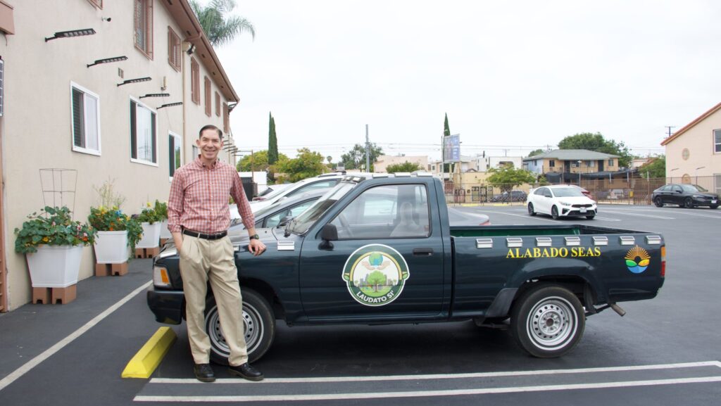 El padre Ricardo González, SVD, párroco de la iglesia Nuestra Señora de Lourdes, en el este de Los Ángeles, posa junto a su camioneta Laudato Si’, que utiliza para transportar desde plantas hasta ropa y muebles. (Kimmy Chacón)