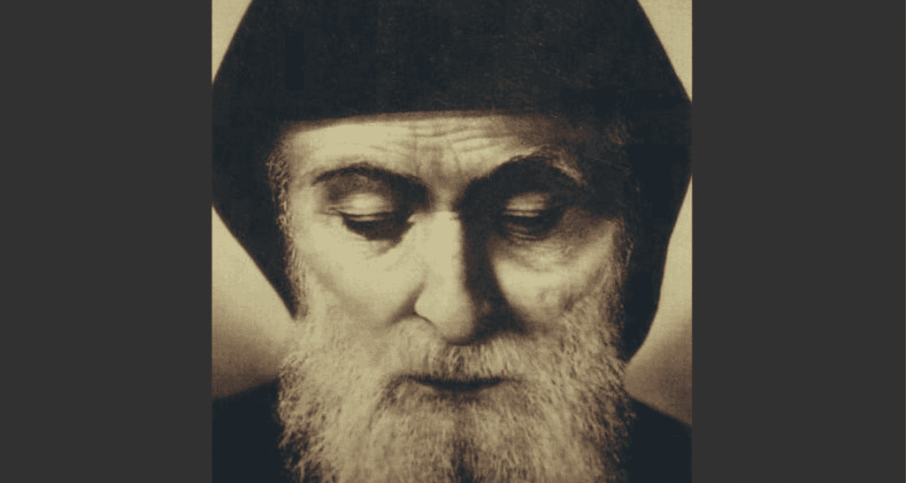 Close-up portrait of an elderly man with a long beard, wearing a dark hat, eyes closed and looking downward.