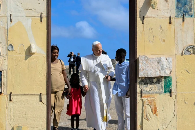 Religious leader in white robes walking with two children and a woman through a stone gate against a bright blue sky.