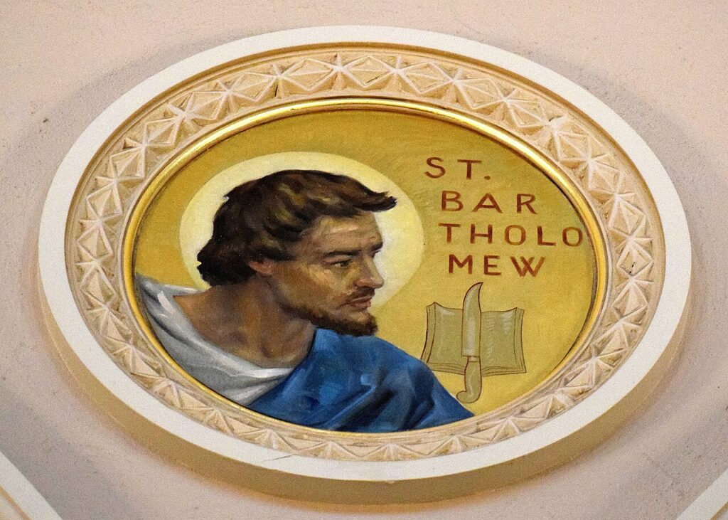 Oval decorative plaque featuring a bearded saint in blue robe with a halo, facing left; inscription reads 'ST. BARTHO MEW' with a book and knife motif nearby.