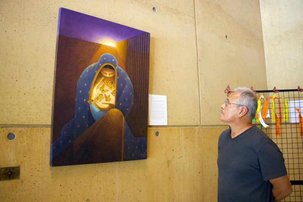 El artista Lalo García observa su pintura “La Virgen Monarca, protectora de los migrantes”, una de las tres obras que eligió para exhibir junto a las cintas de oración. (Kimmy Chacon)