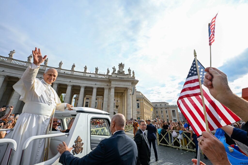El papa León XIV saluda a visitantes y peregrinos desde el papamóvil mientras recorre la plaza de San Pedro, en el Vaticano, antes de su audiencia general semanal del 7 de octubre de 2026. En la imagen se observa una bandera de Estados Unidos. (Foto CNS/Vatican Media)
